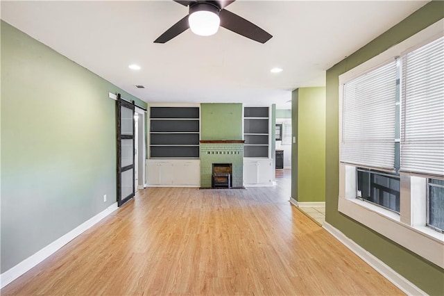 unfurnished living room featuring a barn door, light hardwood / wood-style flooring, and a healthy amount of sunlight