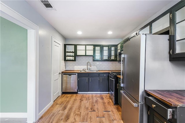 kitchen with sink, butcher block countertops, decorative backsplash, light hardwood / wood-style floors, and stainless steel appliances