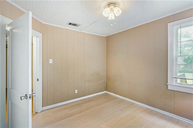 spare room with wood walls, plenty of natural light, ceiling fan, and light wood-type flooring