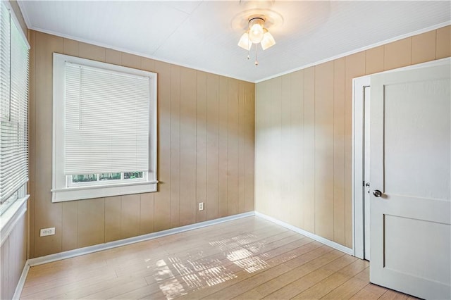 empty room featuring ceiling fan, light hardwood / wood-style flooring, and wooden walls