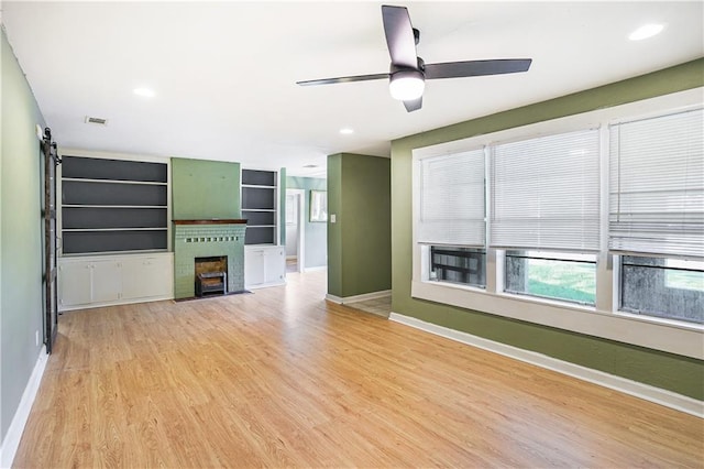 unfurnished living room featuring light hardwood / wood-style flooring, ceiling fan, and a barn door