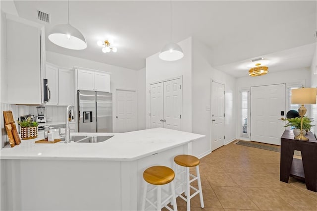 kitchen featuring a peninsula, stainless steel fridge, light countertops, and white cabinets