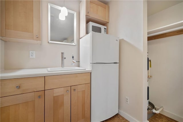 kitchen featuring white appliances, light brown cabinetry, sink, and hanging light fixtures