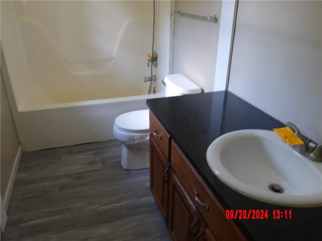 full bathroom with hardwood / wood-style floors, washtub / shower combination, vanity, and toilet