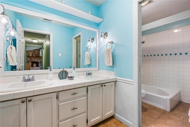 full bathroom with a stone fireplace, tile patterned flooring, a textured ceiling, vanity, and tiled shower / bath