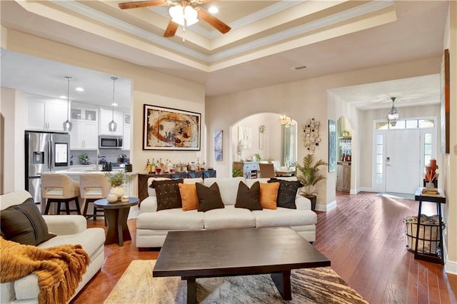 living room featuring dark wood-type flooring, crown molding, and a raised ceiling