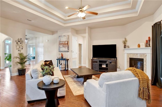 living room featuring ceiling fan, a fireplace, ornamental molding, dark hardwood / wood-style flooring, and a raised ceiling