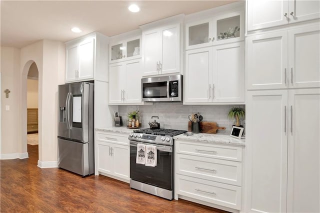 kitchen with white cabinetry, backsplash, light stone counters, stainless steel appliances, and dark wood-type flooring