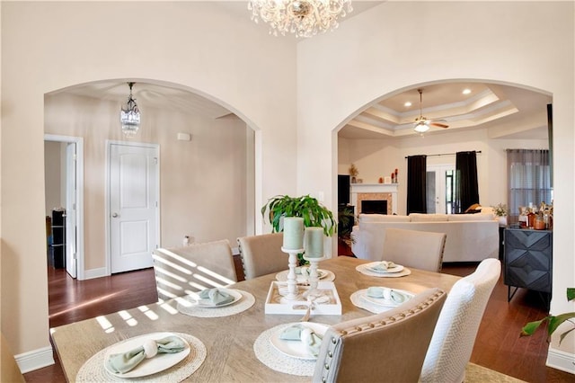 dining space featuring dark wood-type flooring, a tray ceiling, ceiling fan with notable chandelier, and crown molding