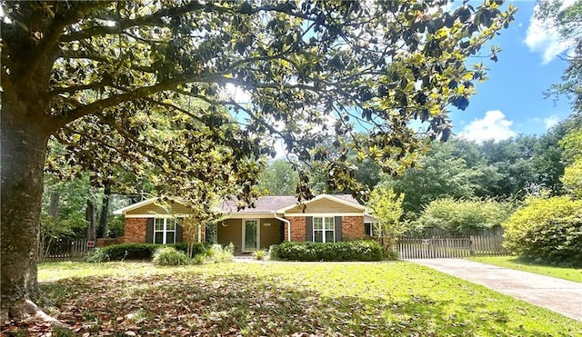 ranch-style home featuring brick siding, fence, driveway, and a front lawn