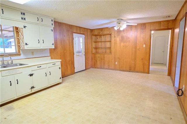 kitchen featuring ceiling fan, sink, white cabinetry, and wood walls