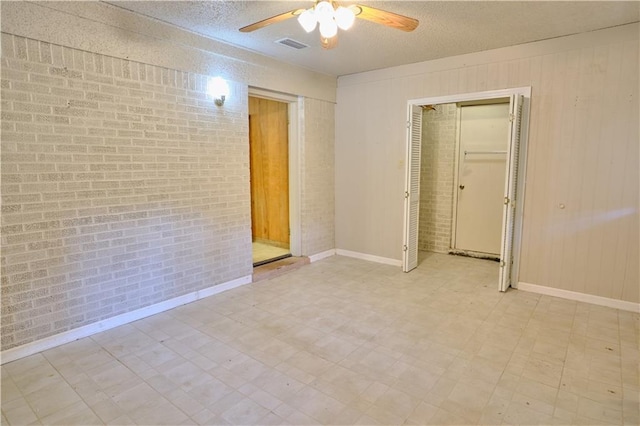 unfurnished bedroom featuring a textured ceiling, light tile patterned floors, a closet, ceiling fan, and brick wall