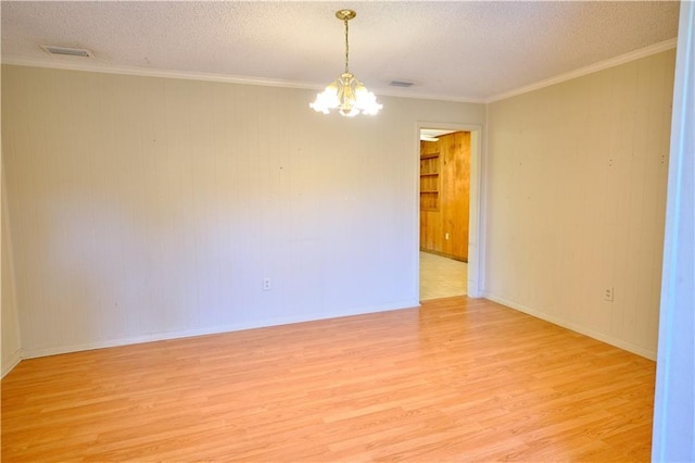 empty room with a textured ceiling, a chandelier, ornamental molding, and light hardwood / wood-style floors