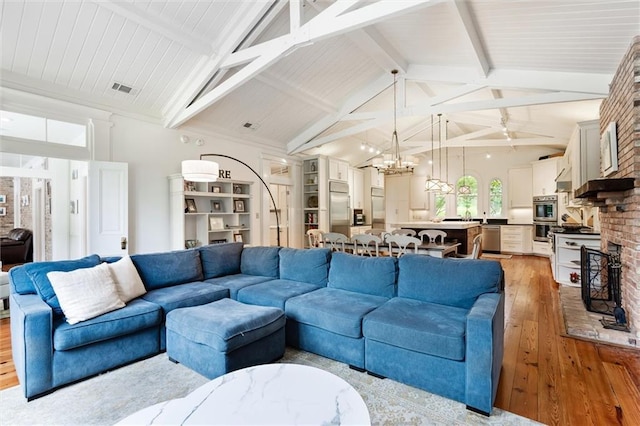 living room with a chandelier, light hardwood / wood-style floors, and vaulted ceiling with beams