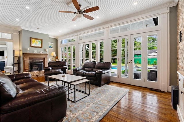 living room featuring french doors, crown molding, ceiling fan, a fireplace, and light hardwood / wood-style floors