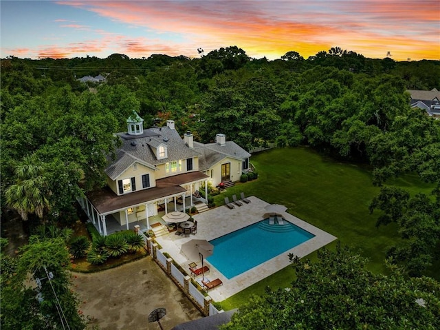 back house at dusk featuring a fenced in pool, a patio area, and a lawn