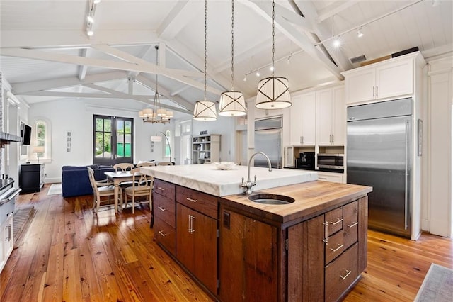 kitchen featuring sink, white cabinetry, stainless steel appliances, an island with sink, and decorative light fixtures