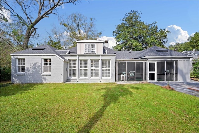 back of house featuring driveway, a sunroom, a lawn, and brick siding