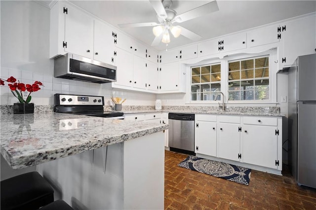 kitchen with decorative backsplash, a peninsula, brick floor, stainless steel appliances, and a sink