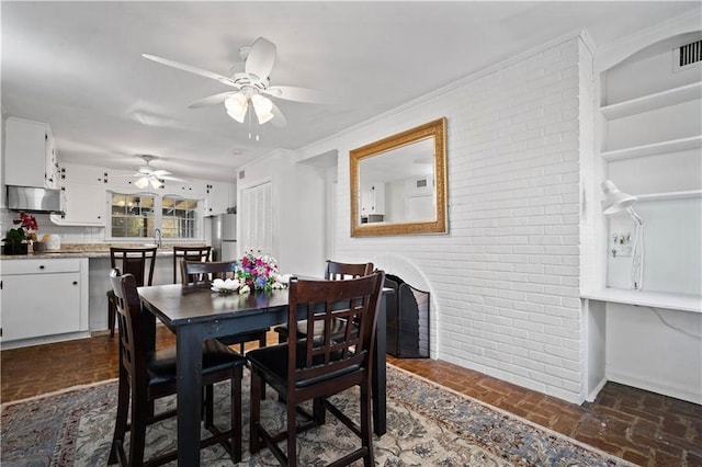 dining area with brick wall, brick floor, and a ceiling fan