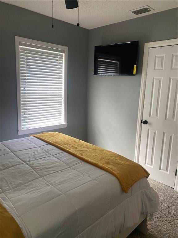 carpeted bedroom featuring a ceiling fan, visible vents, and a textured ceiling