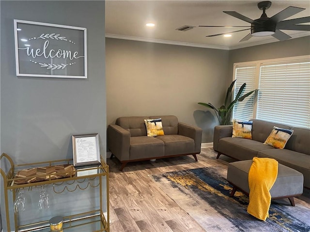 living area featuring crown molding, visible vents, a ceiling fan, wood finished floors, and baseboards