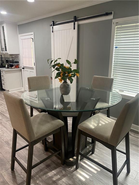 dining space featuring light wood-type flooring, crown molding, recessed lighting, and a barn door