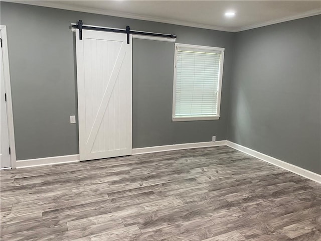 unfurnished bedroom with a barn door, recessed lighting, wood finished floors, baseboards, and ornamental molding