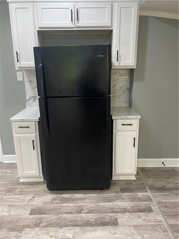 kitchen featuring tasteful backsplash, light countertops, freestanding refrigerator, white cabinets, and baseboards