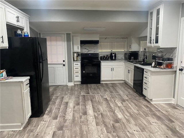 kitchen with black appliances, light wood-style floors, decorative backsplash, and a sink