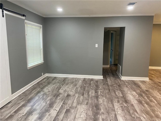 empty room featuring wood finished floors, visible vents, baseboards, and a barn door