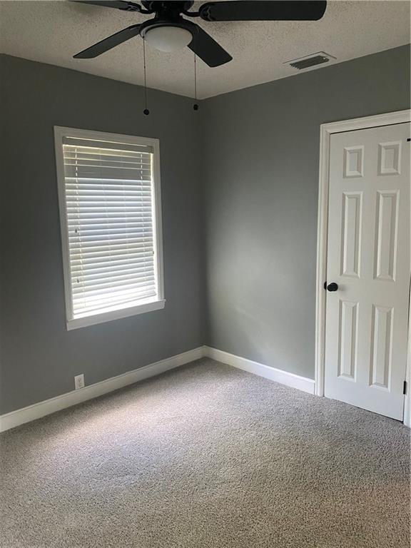 carpeted spare room featuring baseboards, visible vents, and a textured ceiling