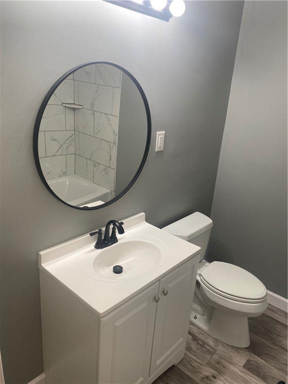 bathroom featuring toilet, baseboards, wood finished floors, and vanity