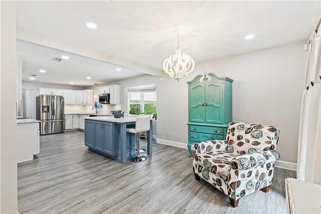 kitchen with stainless steel appliances, hanging light fixtures, light hardwood / wood-style floors, and white cabinetry