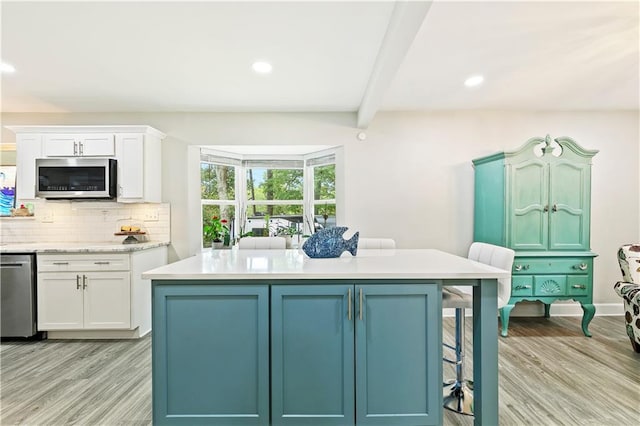 kitchen featuring white cabinets, beam ceiling, appliances with stainless steel finishes, and light wood-type flooring