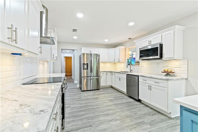 kitchen with white cabinets, appliances with stainless steel finishes, and wall chimney range hood