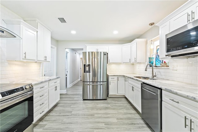 kitchen featuring appliances with stainless steel finishes, white cabinets, backsplash, light wood-type flooring, and sink