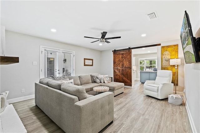 living room featuring ceiling fan, light hardwood / wood-style floors, and a barn door