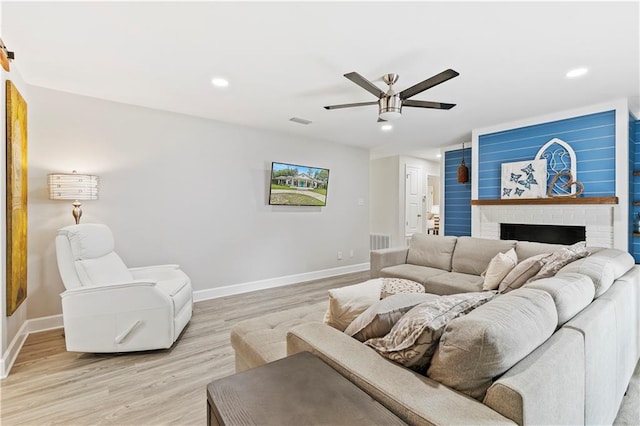 living room with ceiling fan, a fireplace, and light wood-type flooring