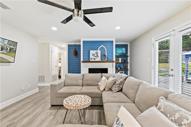 living room with a brick fireplace, light hardwood / wood-style floors, and ceiling fan