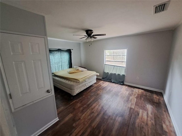 unfurnished bedroom featuring visible vents, ornamental molding, a ceiling fan, wood finished floors, and baseboards