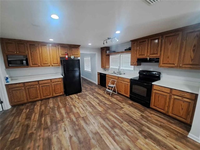 kitchen featuring under cabinet range hood, black appliances, light countertops, and dark wood-style flooring