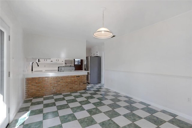 kitchen featuring pendant lighting, sink, kitchen peninsula, stainless steel fridge, and white cabinetry