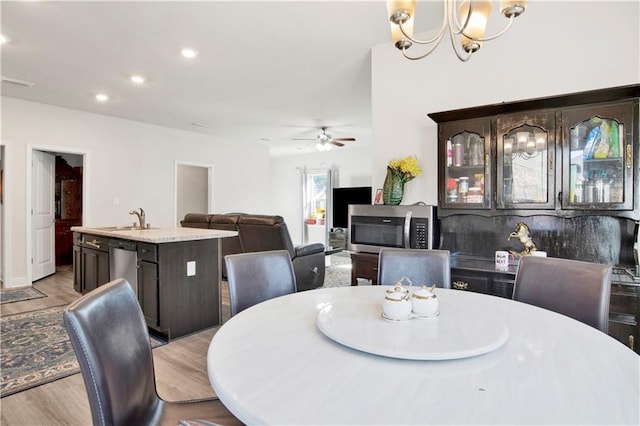 dining room with ceiling fan with notable chandelier, sink, and light hardwood / wood-style flooring