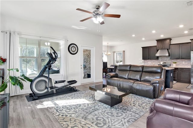 living room with plenty of natural light, ceiling fan with notable chandelier, and light wood-type flooring