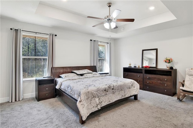 carpeted bedroom with ceiling fan, a tray ceiling, and multiple windows