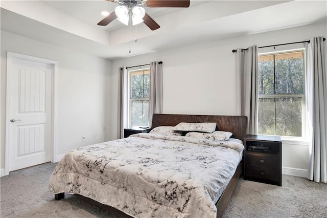 carpeted bedroom featuring multiple windows, ceiling fan, and a tray ceiling