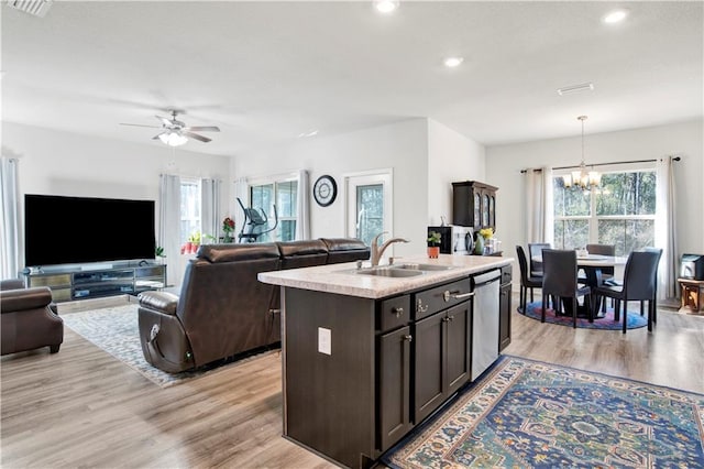 kitchen featuring sink, light hardwood / wood-style flooring, dishwasher, hanging light fixtures, and a center island with sink