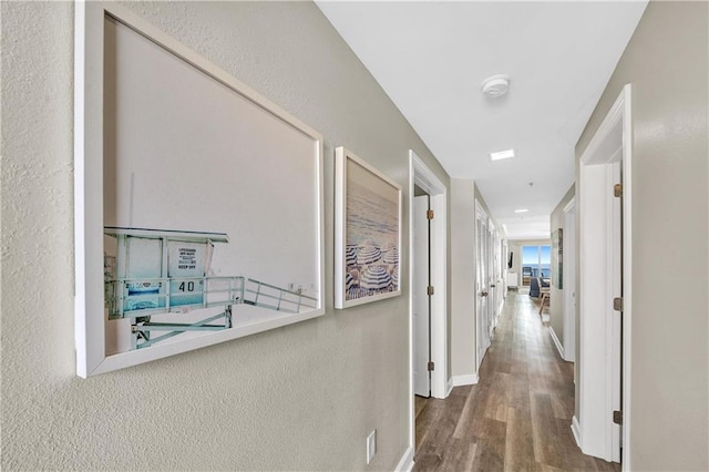 corridor featuring baseboards, a textured wall, and wood finished floors