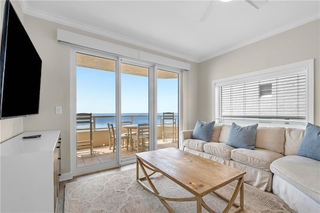 living room with a water view, light wood-type flooring, baseboards, ceiling fan, and ornamental molding